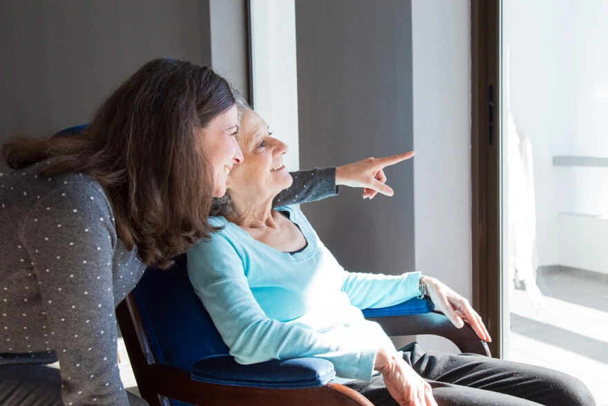 Woman supporting elderly patient at home during recovery, showing care, connection, and positive aftercare environment
